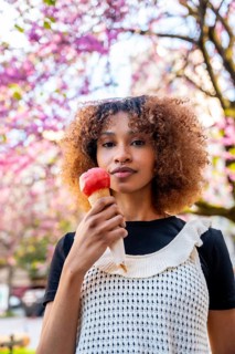 Stylish young woman savoring a strawberry ice cream cone against a backdrop of blooming pink trees