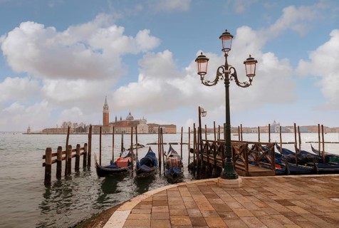 Picturesque Venetian scene with gondolas lined up along the dock and an ornate lamp post, set