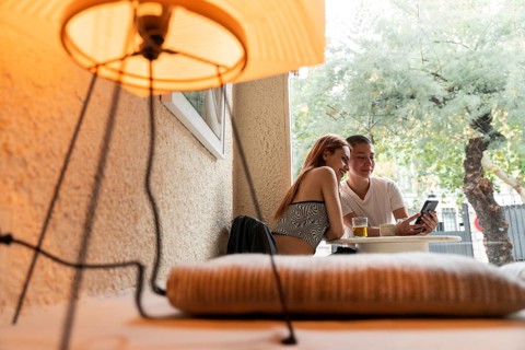 A lesbian couple shares a joyful moment at an outdoor cafe, enjoying drinks and looking at a