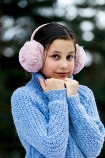 A young girl in a blue knitted sweater and pink earmuffs enjoys a snowy day. The cozy winter attire