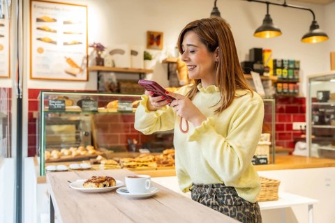 Woman capturing a delicious cinnamon roll and coffee with her smartphone, sharing a moment of