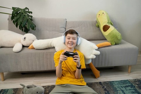 A cheerful boy wearing headphones plays video games with a controller in a cozy living room.