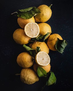 A rustic arrangement of fresh lemons, including a cut lemon revealing its juicy interior, sits atop