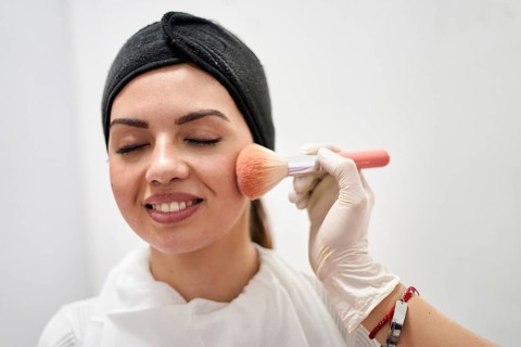 A beauty therapist applies makeup to a client's face in a modern salon. The setting emphasizes