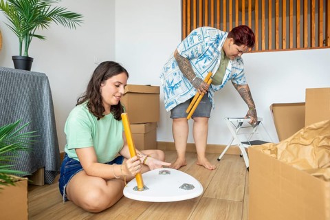 Lesbian friends works together to assemble furniture in their new home. Surrounded by boxes, they