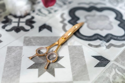 Gold plated professional hairdressing shears on modern patterned gray and white tile floor in a