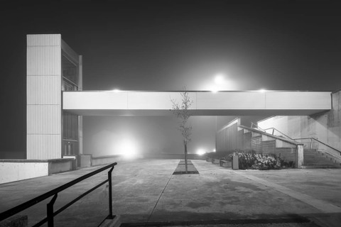 A quiet, atmospheric urban landscape featuring a modern elevator enveloped in mist and fog,