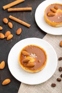 Sweet tartlets with almonds and caramel cream with cup of coffee on a black concrete background and