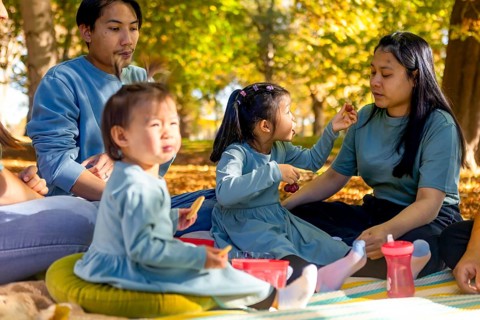 An Asian family enjoys a joyful autumn picnic in a park. Surrounded by vibrant fall colors, they