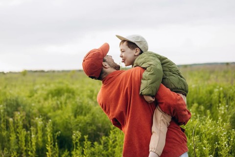 A dad and his young son enjoy a walk through a lush green field, creating joyful memories together.