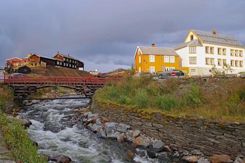 Historic buildings next to a fast-flowing river, illuminated by evening light, mining, Roeros,