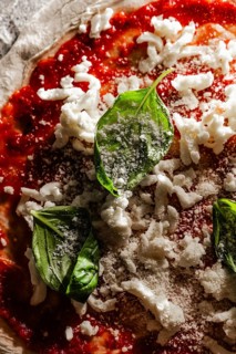 A close up of pizza dough with vibrant tomato sauce, topped with fresh basil leaves and grated