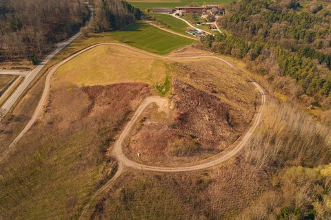 Aerial view shows winding roads over a hill surrounded by fields and trees, old deposit in front of