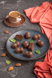 Chocolate candies with almonds and a cup of coffee on a black concrete background and red textile.