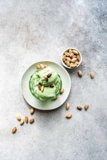 A creamy and homemade scoop of pistachio ice cream sits in a green bowl, surrounded by whole