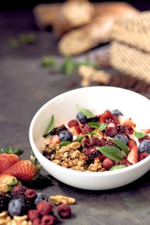 A breakfast natural bowl filled with crunchy granola, fresh strawberries, blueberries, raspberries,