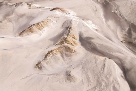 An aerial view captures the rugged desert landscape, showcasing rolling sand dunes and rocky