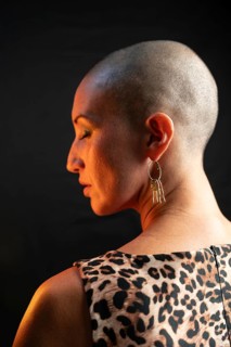 A bald woman is captured from the side wearing a leopard print dress and a gold earring. The
