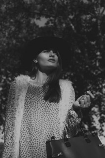 A stylish woman in a fashionable hat and textured coat poses gracefully outdoors, set against a