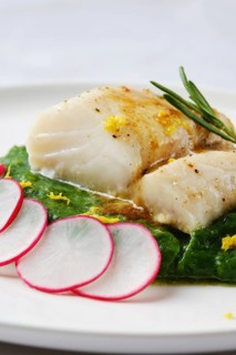 A tender white fish fillet is elegantly placed atop vibrant wilted greens. Fresh radish slices and