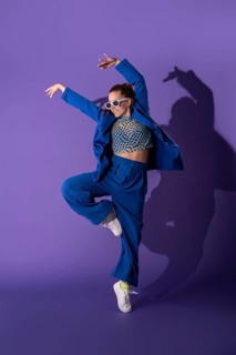 A dynamic young woman dancer elegantly poses against a vivid purple background, clad in a stylish