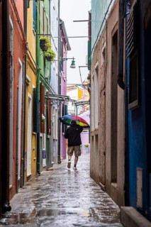 City view of Burano with colourfully painted houses and canals. Rainy weather, people are carrying