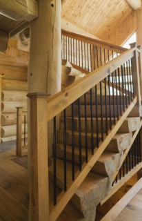 Twisting staircase with wooden and black wrought iron handrail and brown stained half log steps