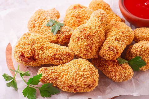 A wooden board holds several golden chicken drumsticks arranged neatly. A small bowl of red dipping