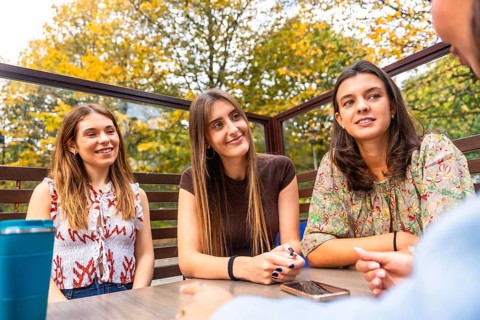 Group of young women friends chatting and laughing at an outdoor cafe terrace on a pleasant autumn