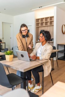 Two businesswomen working together on a laptop, discussing a project in a modern office