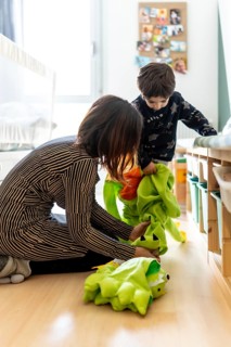 Mother and son playing together at home, preparing dinosaur costume for dress up game in bedroom