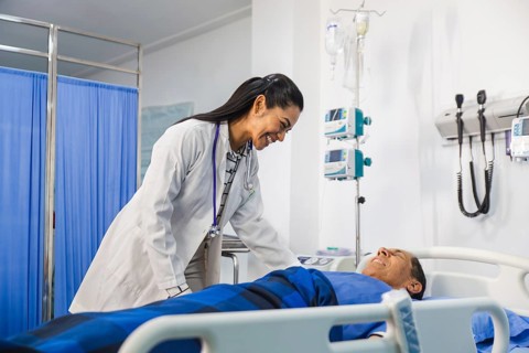 A compassionate female doctor smiles warmly while attending to an elder patient in a hospital room,
