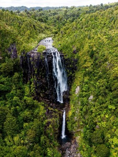 Stunning aerial photo of a towering waterfall cascading down dark volcanic rock, surrounded by