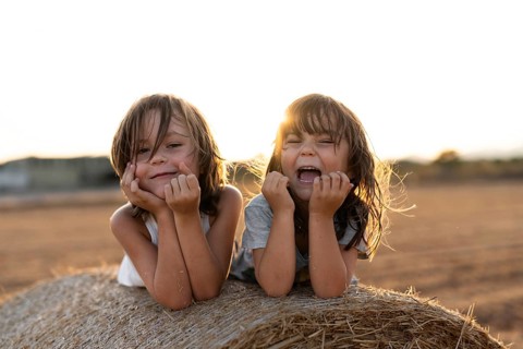 Two happy children lie on a hay bale, bathed in warm sunlight, laughing and enjoying the outdoor
