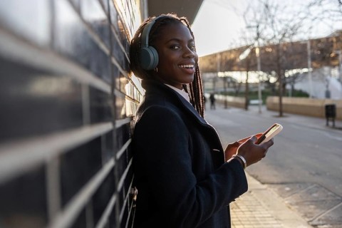An African American businesswoman with braids smiles while taking a break outdoors, listening to