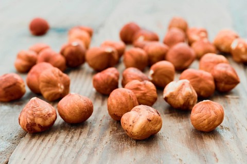 Close-up image of fresh hazelnuts scattered across a rustic wooden surface. The nuts display a