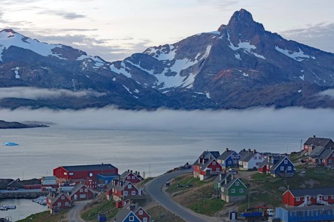 A waterfront village with fog and impressive mountains in the background, Tasilaq, Arctic,