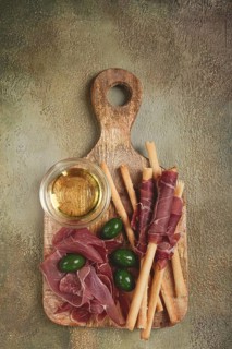 An appetizer of prosciutto, grissini and olives, served on a wooden board, with olive oil