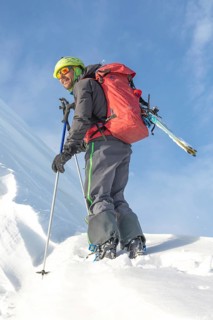 A skier, equipped with a backpack and ski poles, enjoys a sunny day on a snow-covered mountain