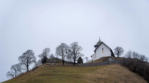 A picturesque white church sits atop a grassy hill, surrounded by bare trees in a hot air balloons