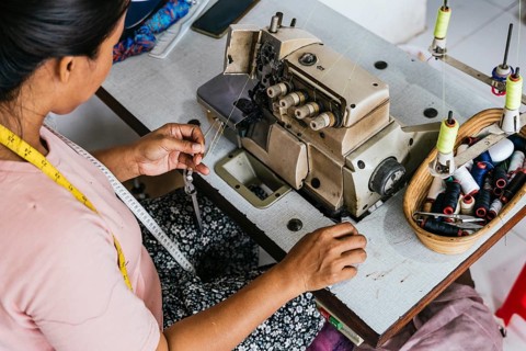 A asian seamstress works at a sewing machine, surrounded by threads and a tape measure. Her focus