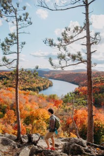 A hiker stands on a rocky outcrop, admiring the stunning autumn foliage and winding river in