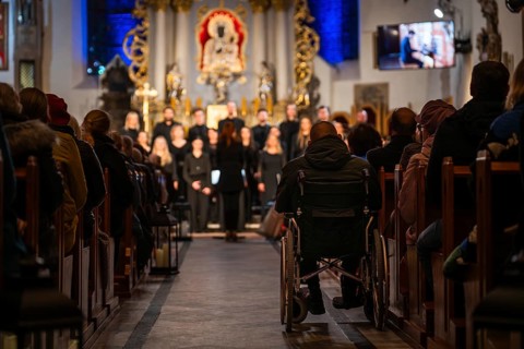Interior of a church during a choir concert with audience in pews and a person in a wheelchair in