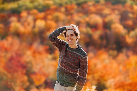 A cheerful man stands amidst the vibrant colors of autumn in Quebec, Canada. The warm tones of red,