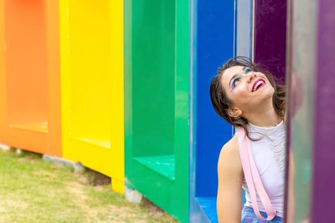 A joyful woman expressing pride and creativity, set against a vibrant rainbow-colored background.