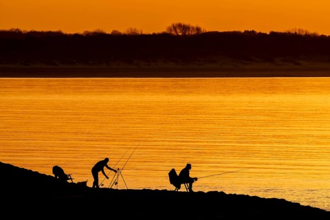 Silhouette of two recreational anglers, fishermen with several fishing rods angling at sunset