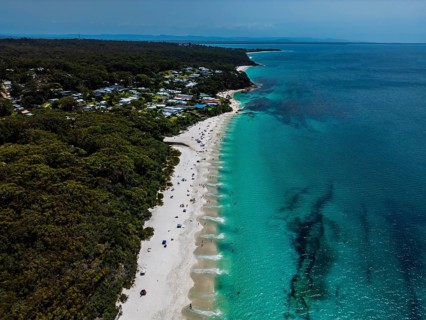 Aerial view of a peaceful beach with turquoise waters and lush forest surrounding a small coastal