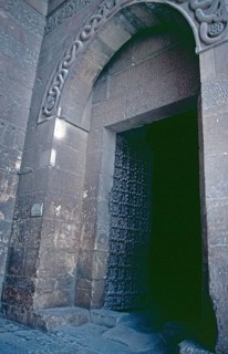 Portal, wrought-iron Tor tor, above it entwined snake bodies with dragon heads in the arch,