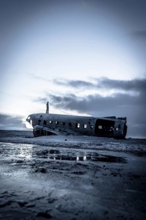 A man stands on a beach next to a large, old airplane that has crashed into the water
