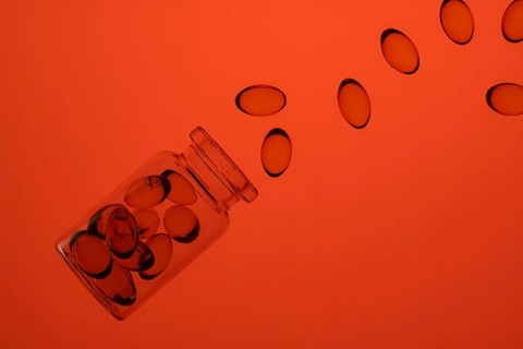 A close-up shot captures colorful omega-3 and vitamin D capsules cascading out of a transparent jar